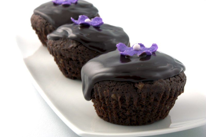 Deep Chocolate Brownie Cupcake A close up photo of 3 chocolate brownie cupcake with a purple flower and a purple ribbon.