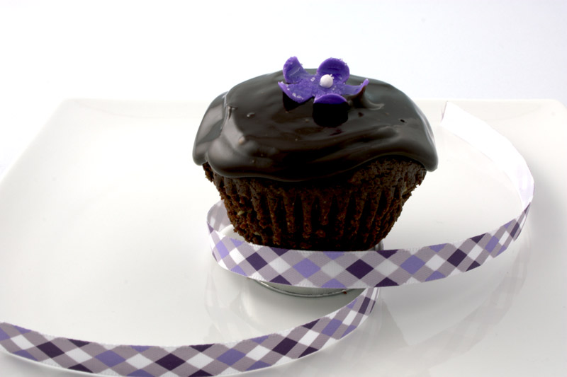 Deep Brownie Chocolate Cupcake A close up photo of a chocolate brownie cupcake with a purple flower and a purple ribbon.