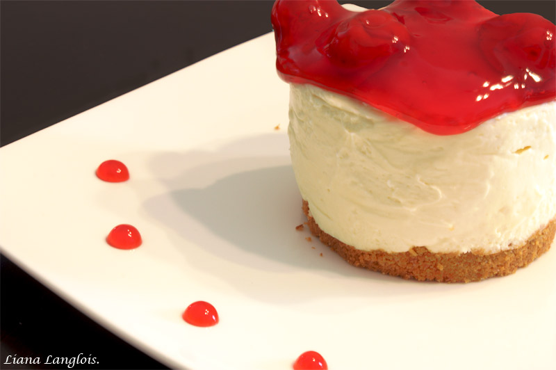 Cheesecake A close up photo of one cheesecake dessert with cherry topping on top of a white dish with a row of sauce drops on the plate.