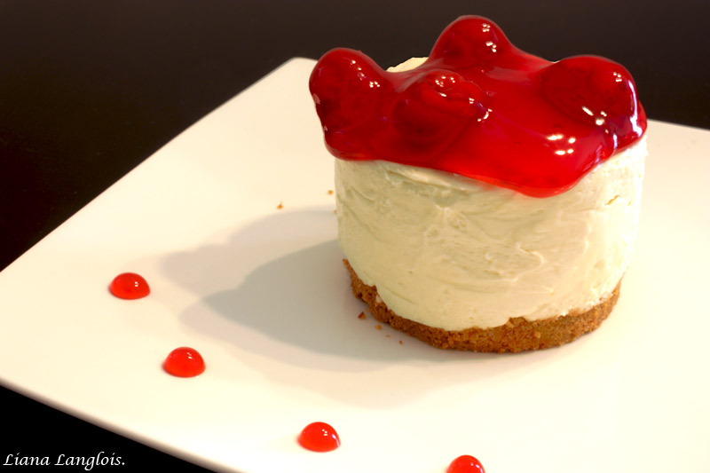 Cheesecake A close up photo of an individual cheesecake dessert with cherry topping on top of a white plate with red cherry sauce drops.