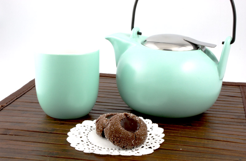 Chocolate Thumbprints A photo of 2 chocolate thumbprints on a white doilie with a turquoise chinese tea pot and teacup on a brown wooden placemat.
