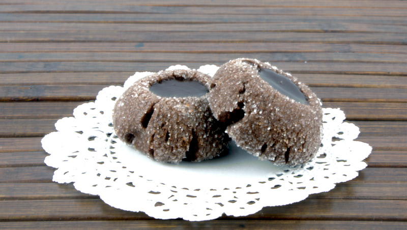 Chocolate Thumbprints A close up photo of 2 chocolate thumbprints on a white doilie placed on a wooden placemat.