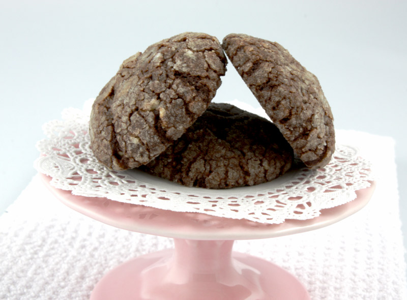 Dark Chocolate-Almond Crackles A close up photo of 3 dark chocolate-almond crackles on a mini pink cake stand on a white tea towel.