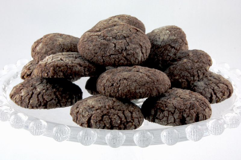 Dark Chocolate-Almond Crackles A close up photo of dark chocolate-almond crackles on a glass cake stand.