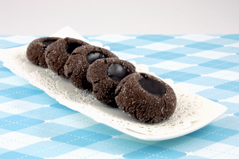Chocolate Thumbprints A close up photo of chocolate thumbprints on a white dish with white doilie on a blue patterned sheet of paper.
