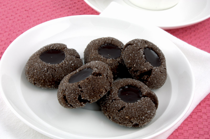 Chocolate Thumbprints A close up photo of chocolate thumbprints on a white dish on a pink napkin with a white cup and saucer.