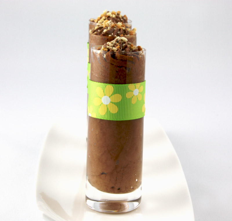 Gordon Ramsay Four-Minute Chocolate Mousse A close up photo of three chocolate mousse in individual shot glasses (a yellow & green ribbon tied around each glass) on a rectangular white dish.