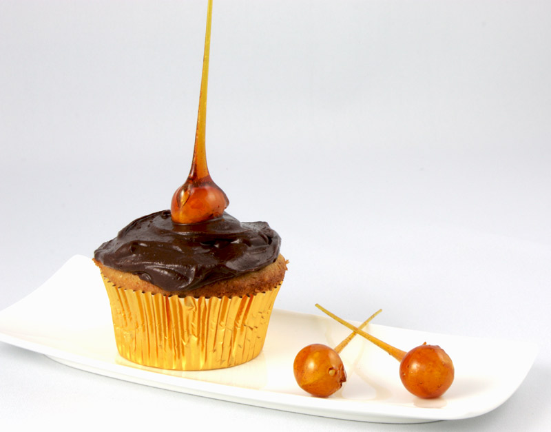Candied-Hazelnut Cupcakes A close up photo of a candied-hazelnut cupcake on a white plate with 2 candied-hazelnuts.