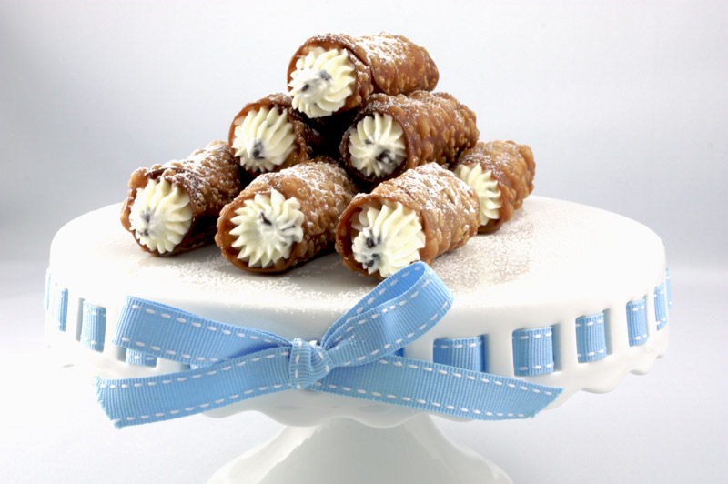 Cannoli Siciliani A photo of Cannoli Siciliani (Italian pastries) on a white cake plate with a blue and white ribbon.