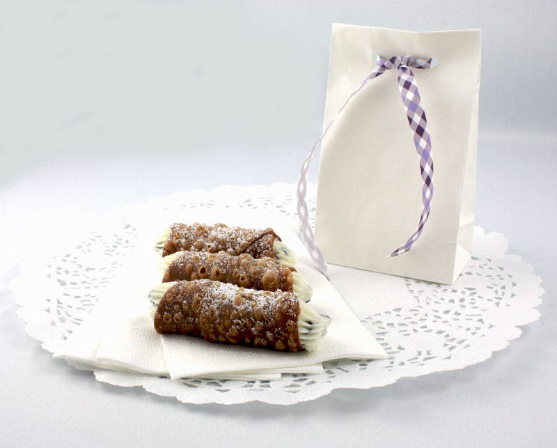 Cannoli Siciliani A photo of Cannoli Siciliani (Italian pastries) sitting on three white napkins on a large white doilie along side a white bag with a purple tied ribbon.