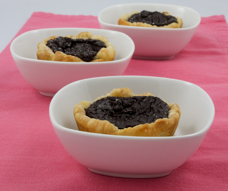 Chocolate Custard Tartlettes A photo of 3 chocolate custard tartlettes in white bowls placed on a pink napkin.