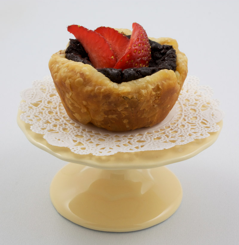 Chocolate Custard Tartlettes A photo of a chocolate custard tartlette with strawberries on a mini yellow cake stand.