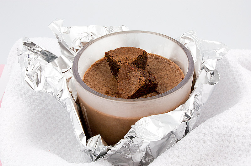 frozen treat recipes, recipe for Donna Hay's double chocolate brownie semifreddo, Italian semifreddo recipes A close up photo of a double chocolate brownie semifreddo dessert served in a clear tumbler garnished with brownie bites, tumbler is wrapped in tin foil, nestled in a white tea towel.