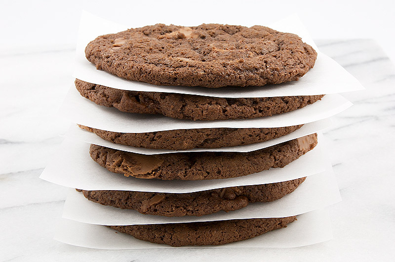 double-chocolate chunk cookies recipe, Martha Stewart cookie recipes, easy recipe for double chocolate chunk cookies, delicious double chocolate cookies A close up photo of stacked double-chocolate chunk cookies separated with squares of parchment paper between each cookie.