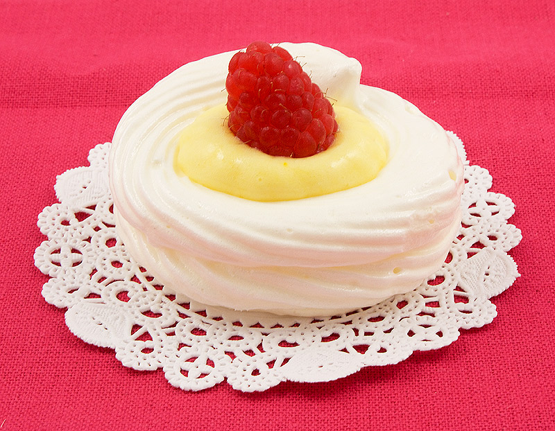 lemon curd meringue nests, meringue nests, meringue cups, easy lemon curd A photo of a lemon curd meringue nest garnished with a raspberry on a white doilie, placed on a pink placemat.