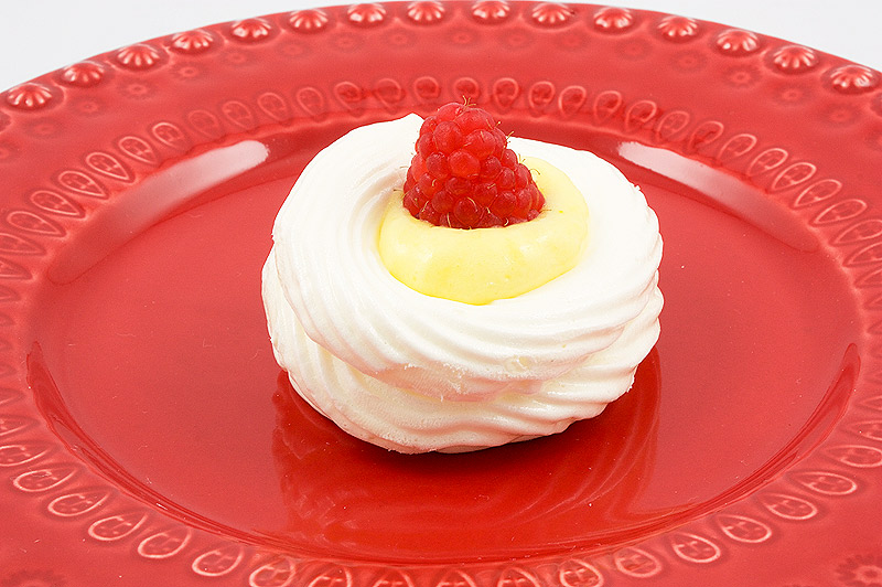 lemon curd meringue nests, meringue nests, meringue cups, easy lemon curd A photo of a lemon curd meringue nest garnished with a raspberry on a red plate.