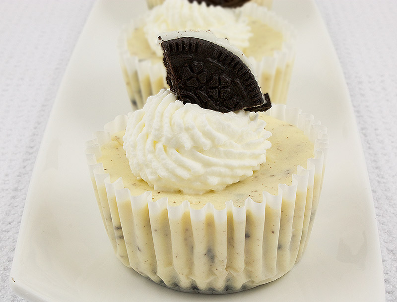 Oreo cookies and cream cheesecakes, Martha Stewart's cookies and cream cheesecakes recipe, easy recipe for Oreo cookies and cream cheesecake cupcakes A photo of 3 Oreo cookies and cream cheesecakes with whipped cream and Oreo cookies on top, placed on a white plate.