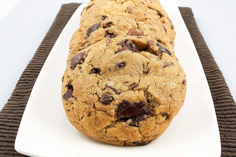 decadent chocolate chip cookies, easy chocolate chip cookie recipe, tips for making the best chocolate chip cookies A photo of Jacques Torres's Secret Chocolate Chip Cookies placed in a row on a white, rectangular dish placed on a dark brown tea towel.