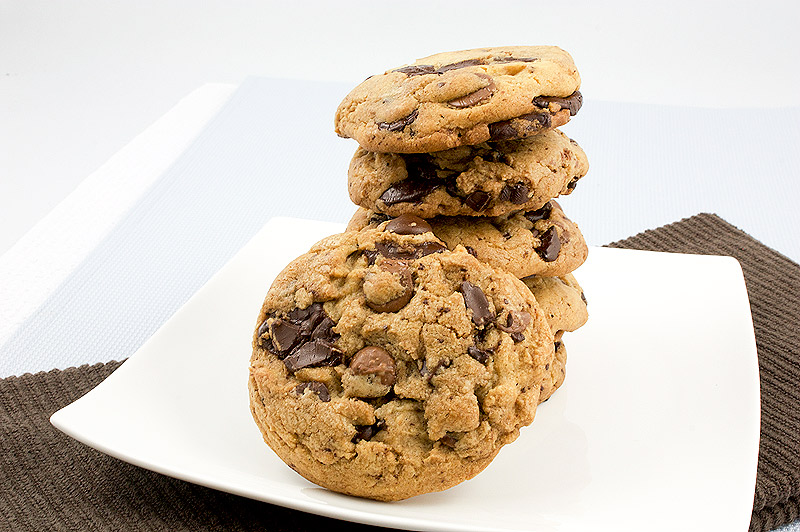 Jacques Torres's secret chocolate chip cookie recipe, Jacques Torres's recipe for chocolate chip cookies, bakery style chocolate chip cookies A photo of a white, square plain containing a stack of freshly baked chocolate chip cookies placed on a brown tea towel.