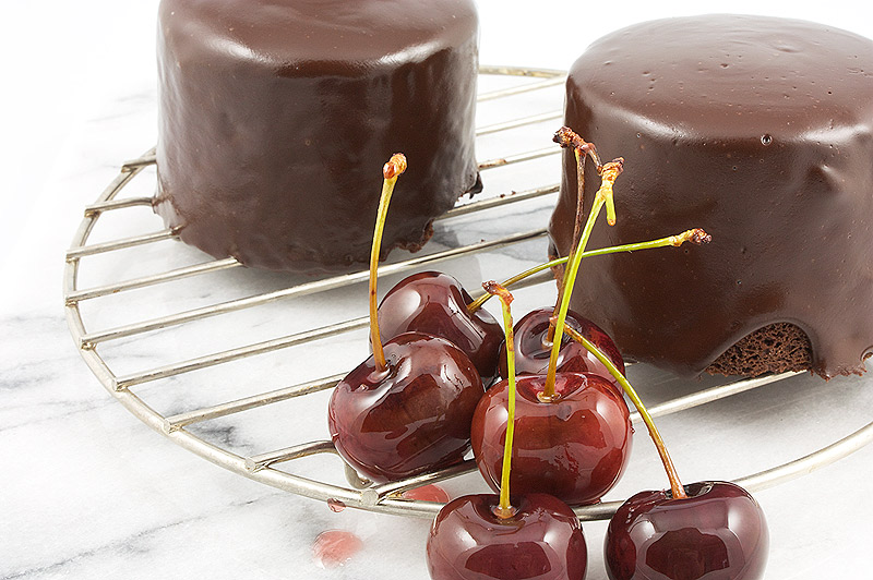 easy recipe for chocolate mud cake, simple dark chocolate ganache icing, easy glazed cherries A close up photo of sweet, glazed cherries and 2 individual sized chocolate mud cakes with ganache glaze.