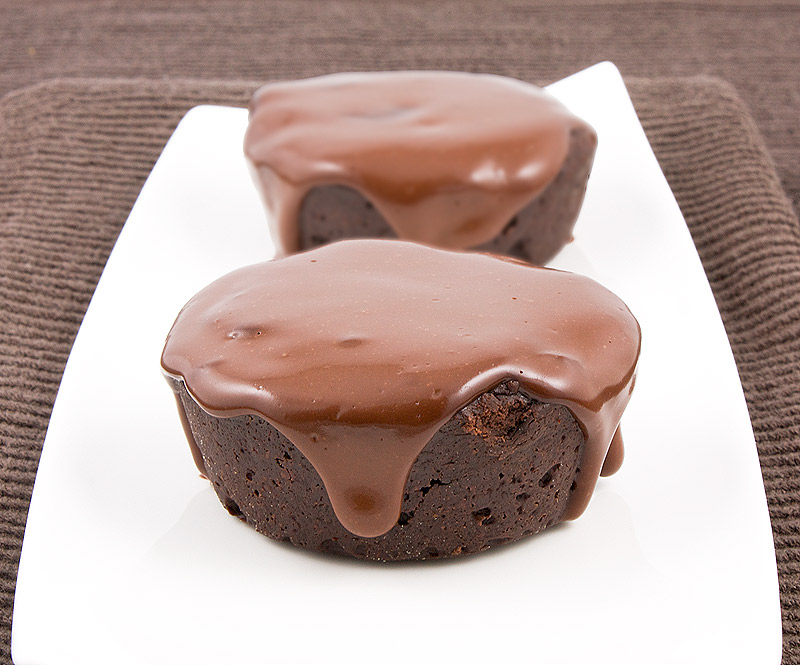 Donna Hay chocolate desserts, Donna Hay's Modern Classics Book 2 dessert recipes, how to make sugared berries, simple chocolate glaze recipe A close up photo of 2 flourless chocolate cakes with chocolate glaze on a white, rectangular plate resting on a chocolate brown tea towel.