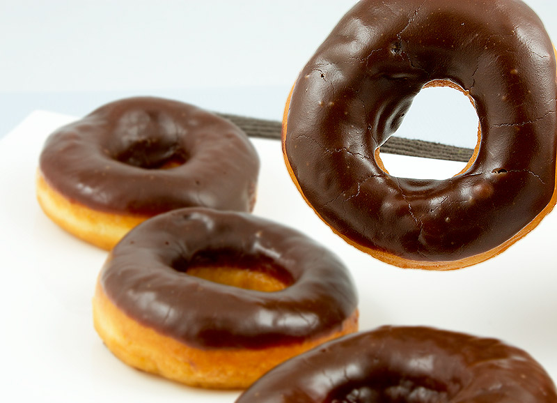 how to make doughnuts at home, doughnut recipe, chocolate doughnut glaze A photo of 4 chocolate glazed doughnuts with one suspended in the air.