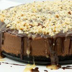 chocolate cheesecake recipe, simple chocolate dessert, easy dessert recipes A close up photo of a chocolate cheesecake with chocolate sauce, butter caramel sauce and toasted hazelnuts.