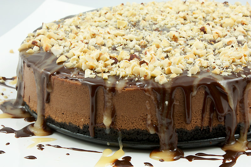 chocolate cheesecake recipe, simple chocolate dessert, easy dessert recipes A close up photo of a chocolate cheesecake with chocolate sauce, butter caramel sauce and toasted hazelnuts.