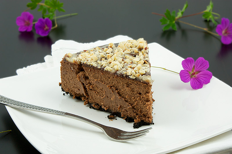 chocolate cheesecake recipe, simple chocolate dessert, easy dessert recipes A photo of a slice of chocolate cheesecake with an Oreo cookie crust topped with chocolate sauce, butter caramel sauce and toasted hazelnuts.