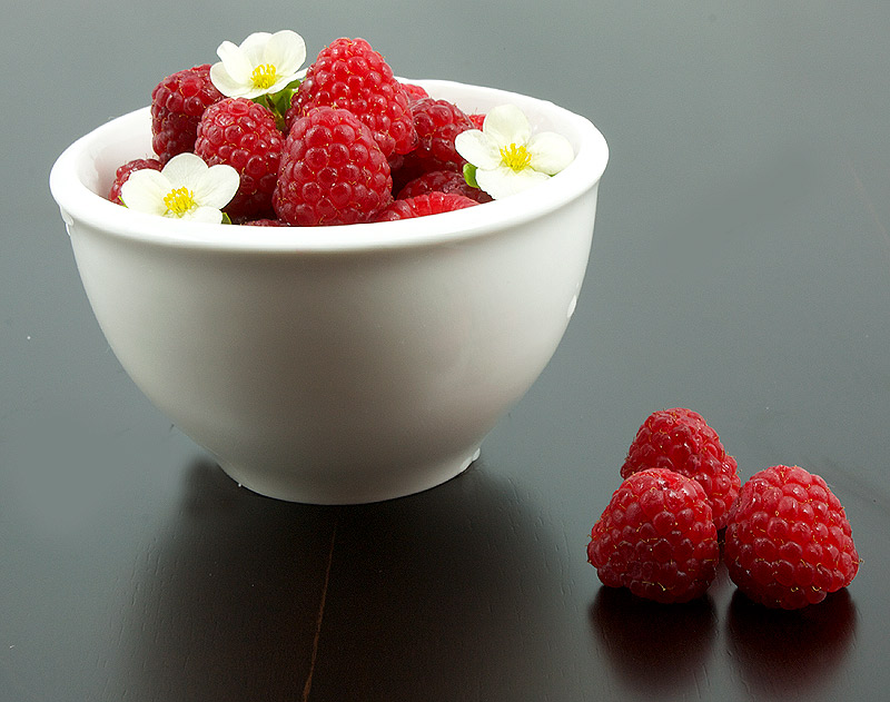 baked cheesecake recipe, caramel sauce recipe, easy chocolate sauce recipes A photo of a bowl of fresh raspberries with a few tiny white flowers.