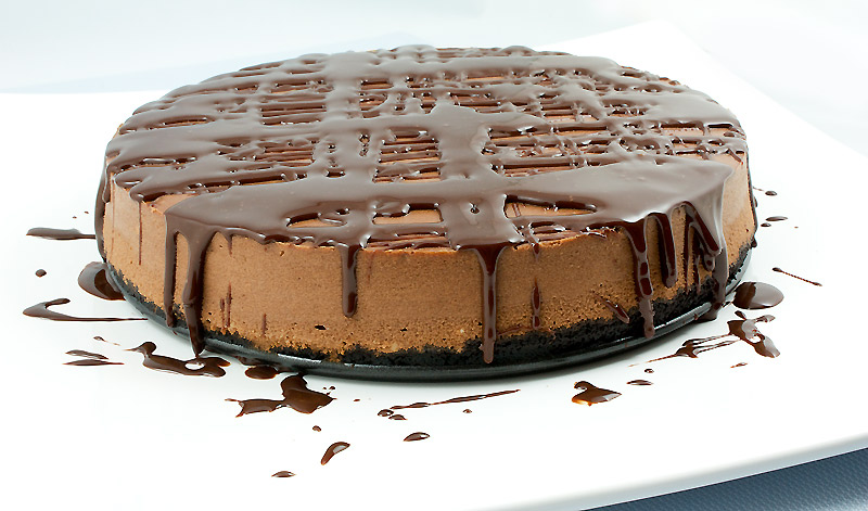baked cheesecake recipe, caramel sauce recipe, easy chocolate sauce recipes A photo of a chocolate cheesecake with Oreo cookie crust topped with chocolate sauce.