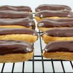 Chocolate Éclairs with Vanilla Bean Crème Pâtissière and Chocolate Ganache Glaze A close up photo of Chocolate Éclairs with Vanilla Bean Crème Pâtissière and Chocolate Ganache Glaze french pastries on a cooling rack.