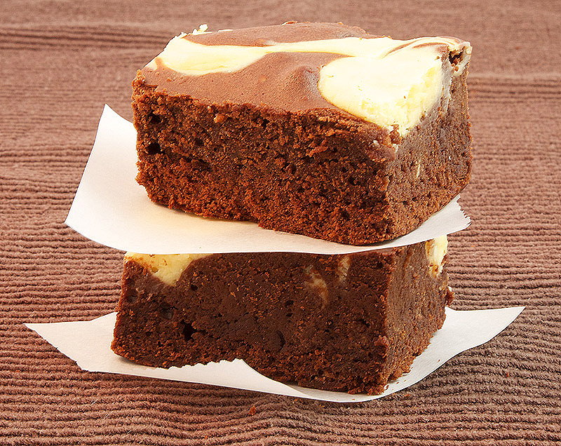 Baileys® Cheesecake Swirl Chocolate Brownies A photo of 2 Baileys® Cheesecake Swirl Chocolate Brownie squares, stacked with pieces of parchment separating the squares.