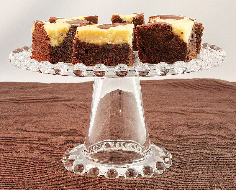 chocolate fudge brownie recipe, cheesecake brownies, Baileys cheesecake recipe, easy chocolate brownies A photo of Baileys® Cheesecake Swirl Chocolate Brownies on a glass cake stand.