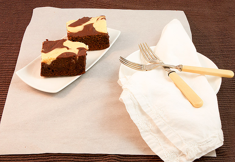 cheesecake brownies, Baileys cheesecake recipe, easy chocolate brownies A photo of 2 Baileys® Cheesecake Swirl Chocolate Brownie squares on a small, rectangular white plate along side 2 dessert plates with a cloth napkin and 2 dessert forks.