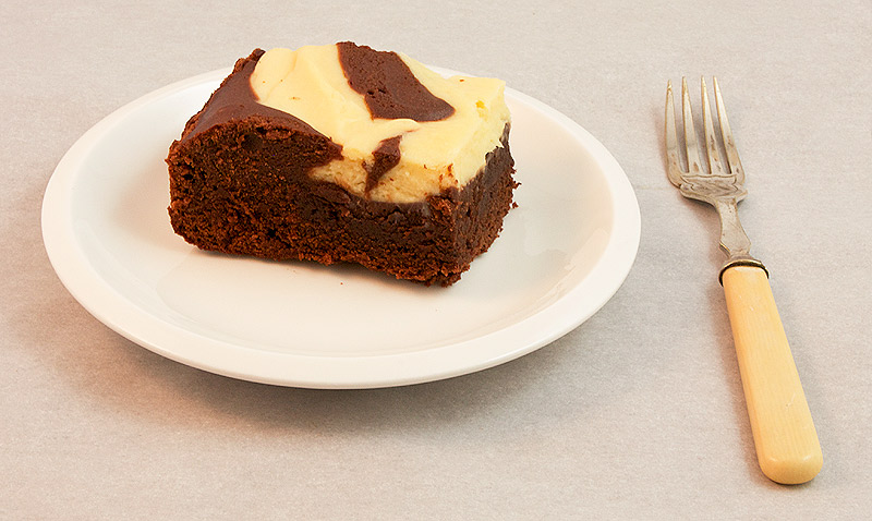 Baileys cheesecake recipes, dark chocolate recipes, chocolate dessert recipes A photo of a Baileys® Cheesecake Swirl Chocolate Brownie square on a small white plate with a dessert fork.