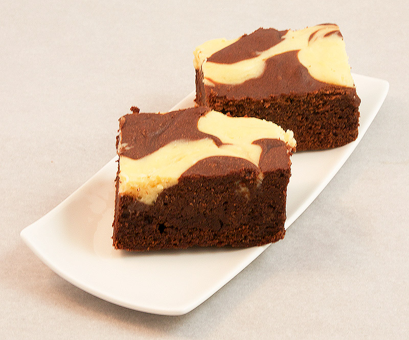 Donna Hay's Cheesecake Swirl Chocolate Brownies A photo of Donna Hay's Cheesecake Swirl Chocolate Brownies placed on a white, rectangular dessert plate.
