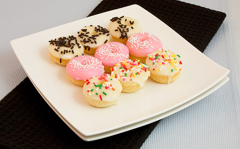 doughnut recipes, cake doughnut recipe, doughnut recipes A photo of a plate of white chocolate baked doughnuts with vanilla glaze and decorated with various sprinkles.
