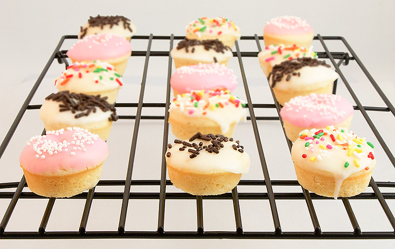 baked doughnut recipe, doughnut glaze, baked donuts A photo of Baked White Chocolate Cake Doughnuts with Vanilla Glaze and decorated with sprinkles on a wire rack.