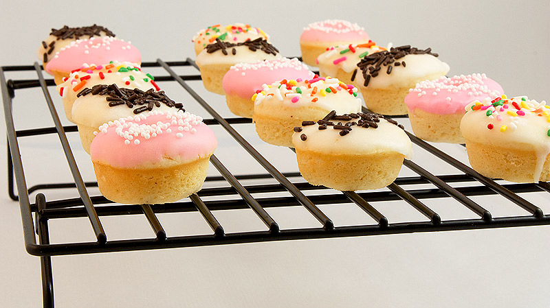 baked doughnut recipe, doughnut glaze, baked donuts A photo of mini baked cake doughnuts with vanilla doughnut glaze and decorated with assorted sprinkles cooling on a wire rack.