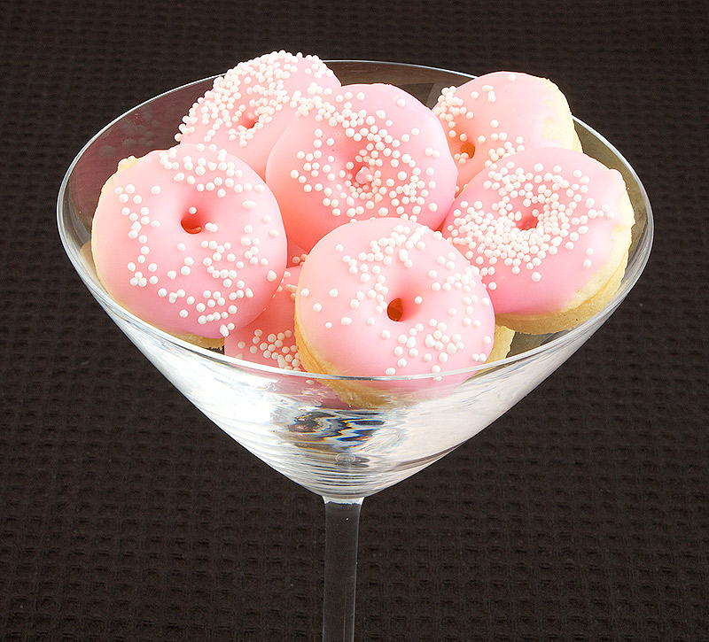 Baked White Chocolate Cake Doughnuts with Vanilla Glaze A photo of Baked White Chocolate Cake Doughnuts with pink Vanilla Doughnut Glaze and decorated with white nonpareils in a clear martini glass.