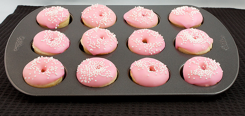 glazed doughnut recipe, donuts recipe, donut glaze A photo of mini doughnuts with pink doughnut glaze and decorated with white nonpareils in a Wilton mini doughnut pan.