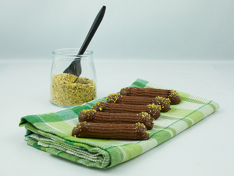 Chocolate Spritz Cookies A photo of Chocolate Spritz Cookies dipped in chocolate and sprinkled with pistachio crumb with a jar of pistachio crumb off to the side.