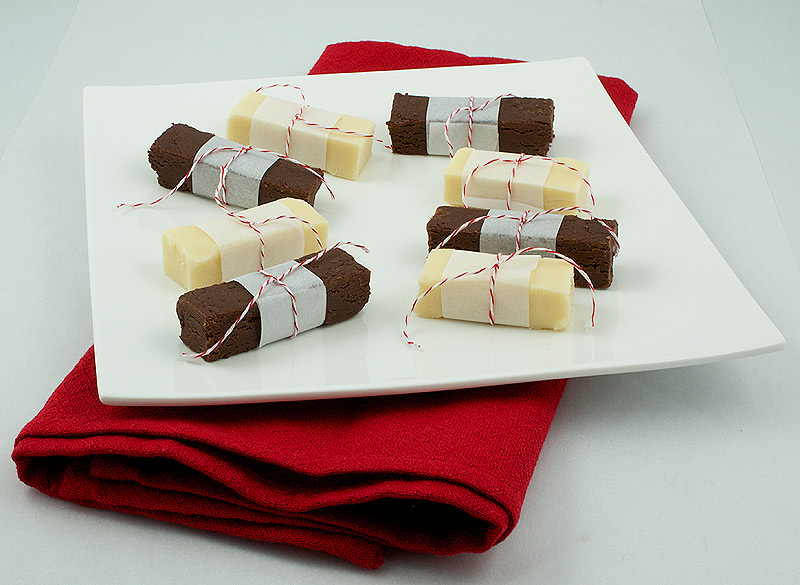 easy holiday recipes, easy fudge recipes, easy chocolate fudge recipe A photo of several pieces of Holiday Fudge cut in bar form and wrapped in non stick baking paper and secured with decorative red and white cooking twine placed on a square white plate.