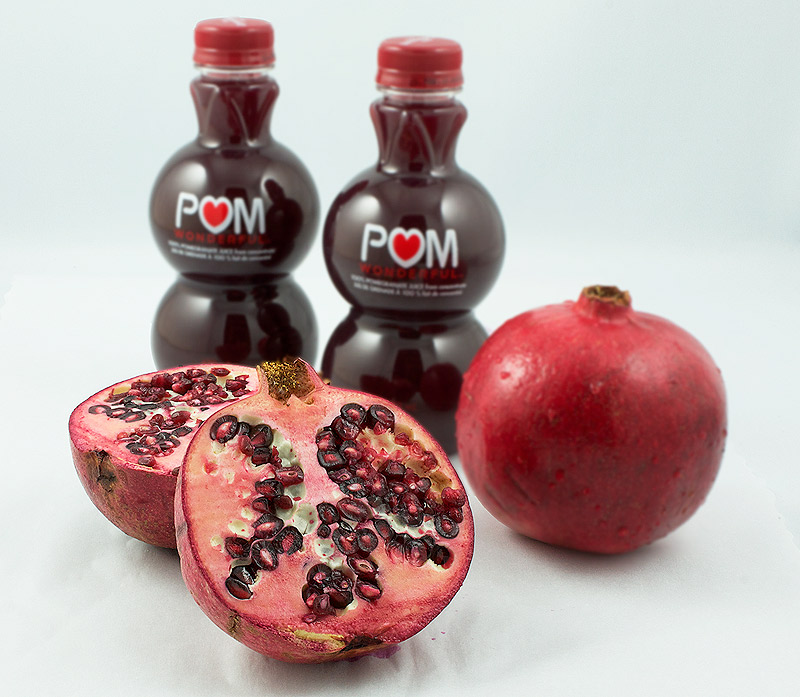 Pom Pomegranate Juice and 2 Fresh Pomegranates A photo of 2 bottles of Pom Pomegranate Juice and 2 Fresh Pomegranates, 1 split in half exposing the pomegranate seeds.