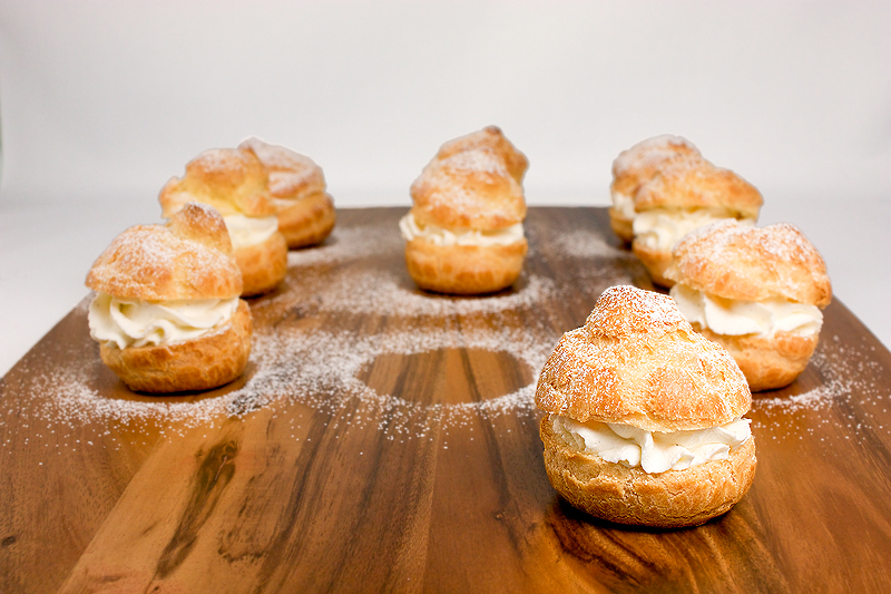 how to make chocolate sauce, choux pastry, choux pastry recipe, chantilly cream recipe A photo of Profiteroles on a wooden cutting board.