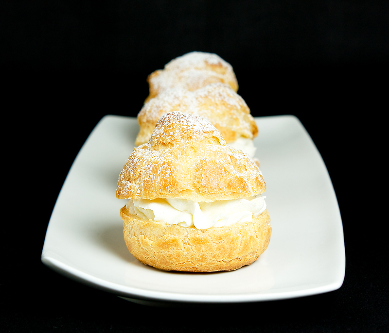 Gordon Ramsay Desserts, profiterole, cream puff recipe, recipe for profiteroles A photo of Profiteroles with Vanilla Crème Chantilly and dusted with icing sugar placed in a row on a white rectangular plate.