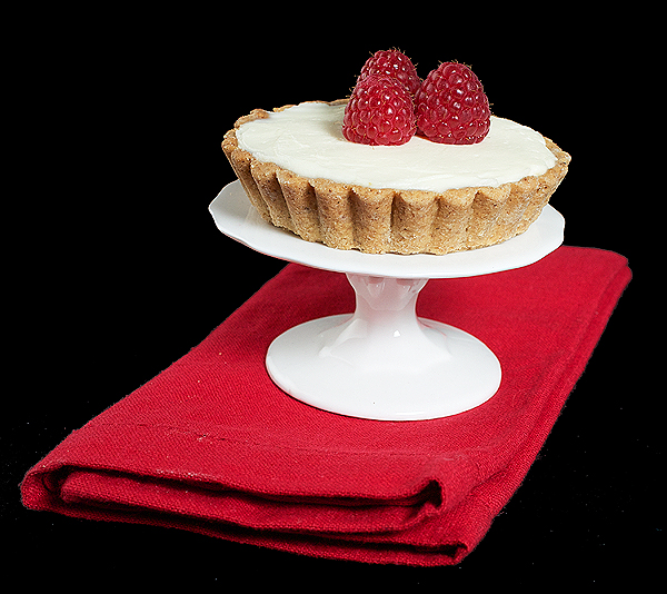 raspberry jam recipes, how to make raspberry jam, sweet shortcrust pastry A photo of a White Chocolate Tart garnished with fresh raspberries on a small cupcake stand.