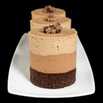 Triple Chocolate Mousse Cakes A photo of 3 Triple Chocolate Mousse Cakes displayed in a row on a white rectangular dish with a black background.