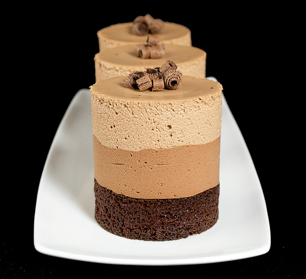 Triple Chocolate Mousse Cakes A photo of 3 Triple Chocolate Mousse Cakes displayed in a row on a white rectangular dish with a black background.